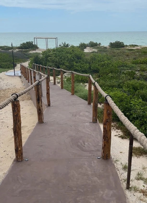Andador hacia la playa con postes de madera y un barandal de cuerda trenzada.