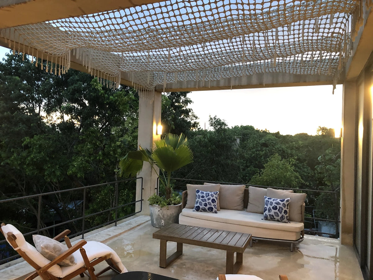 Vista amplia de la terraza con sofá, sillas de madera y cubierta tejida iluminada al atardecer.
