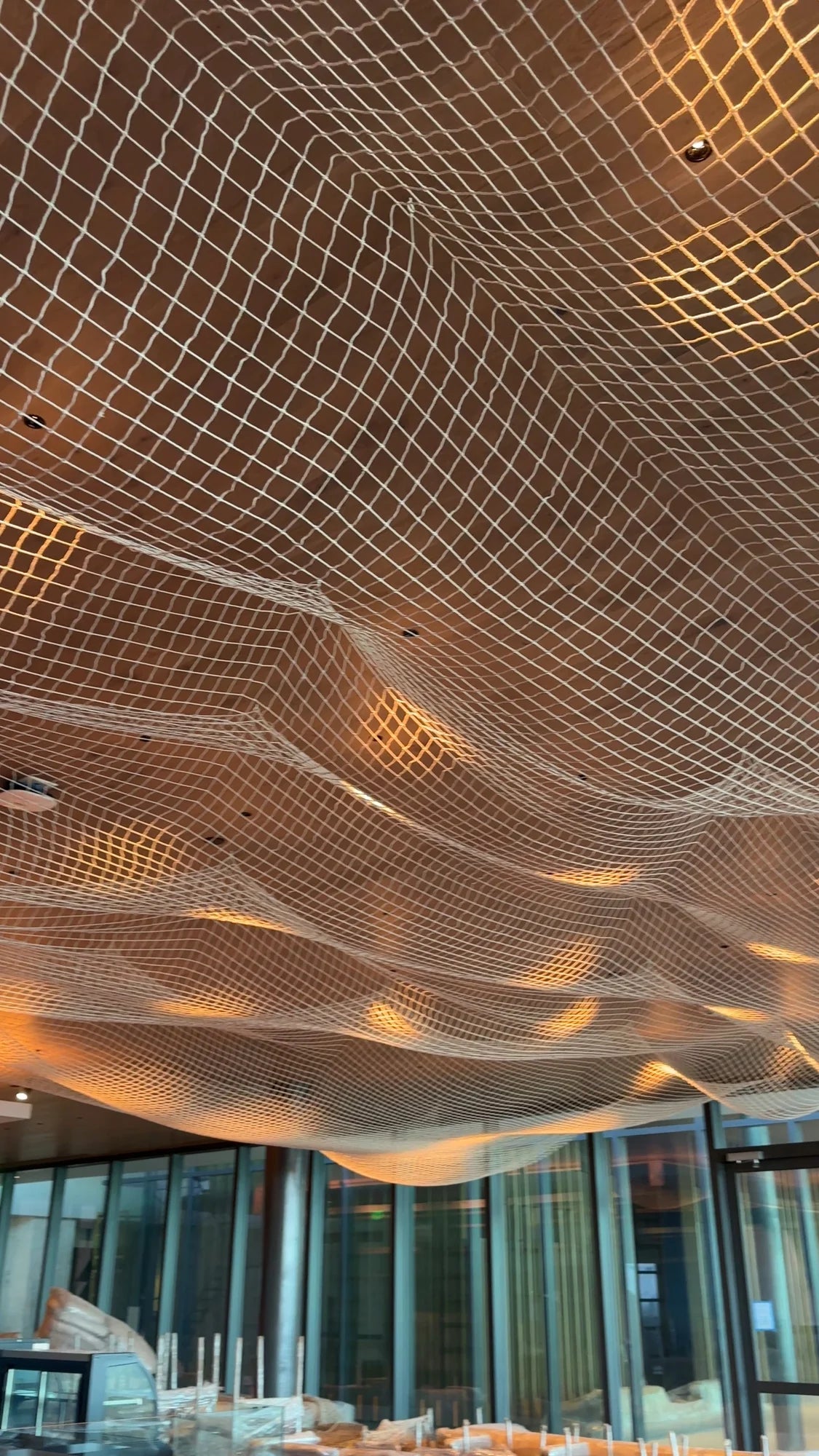 Red clara suspendida en ondas bajo un plafón de madera con iluminación cálida; al fondo se observa mobiliario protegido.