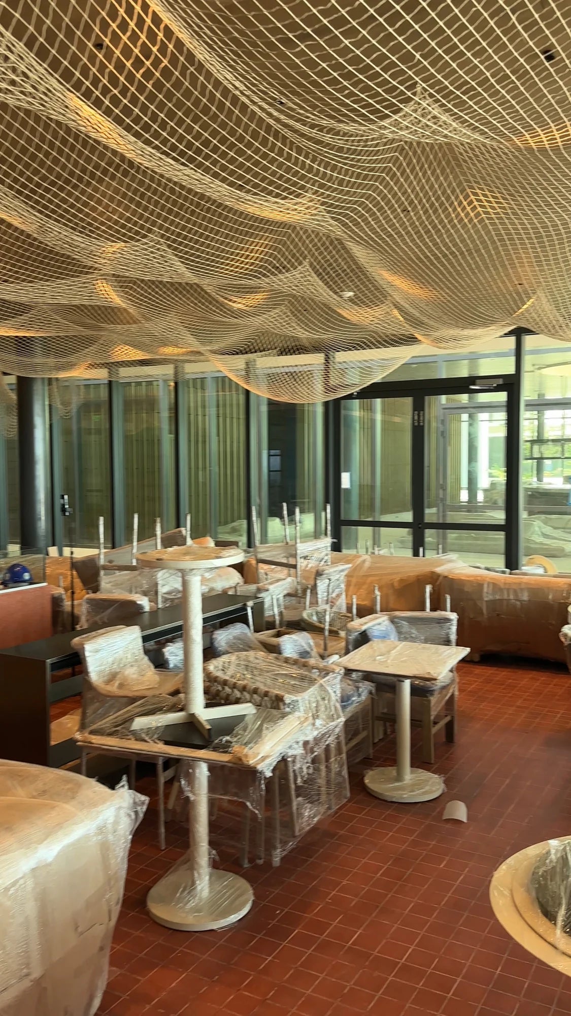 Vista del salón con redes suspendidas sobre mesas y asientos todavía cubiertos con protección.