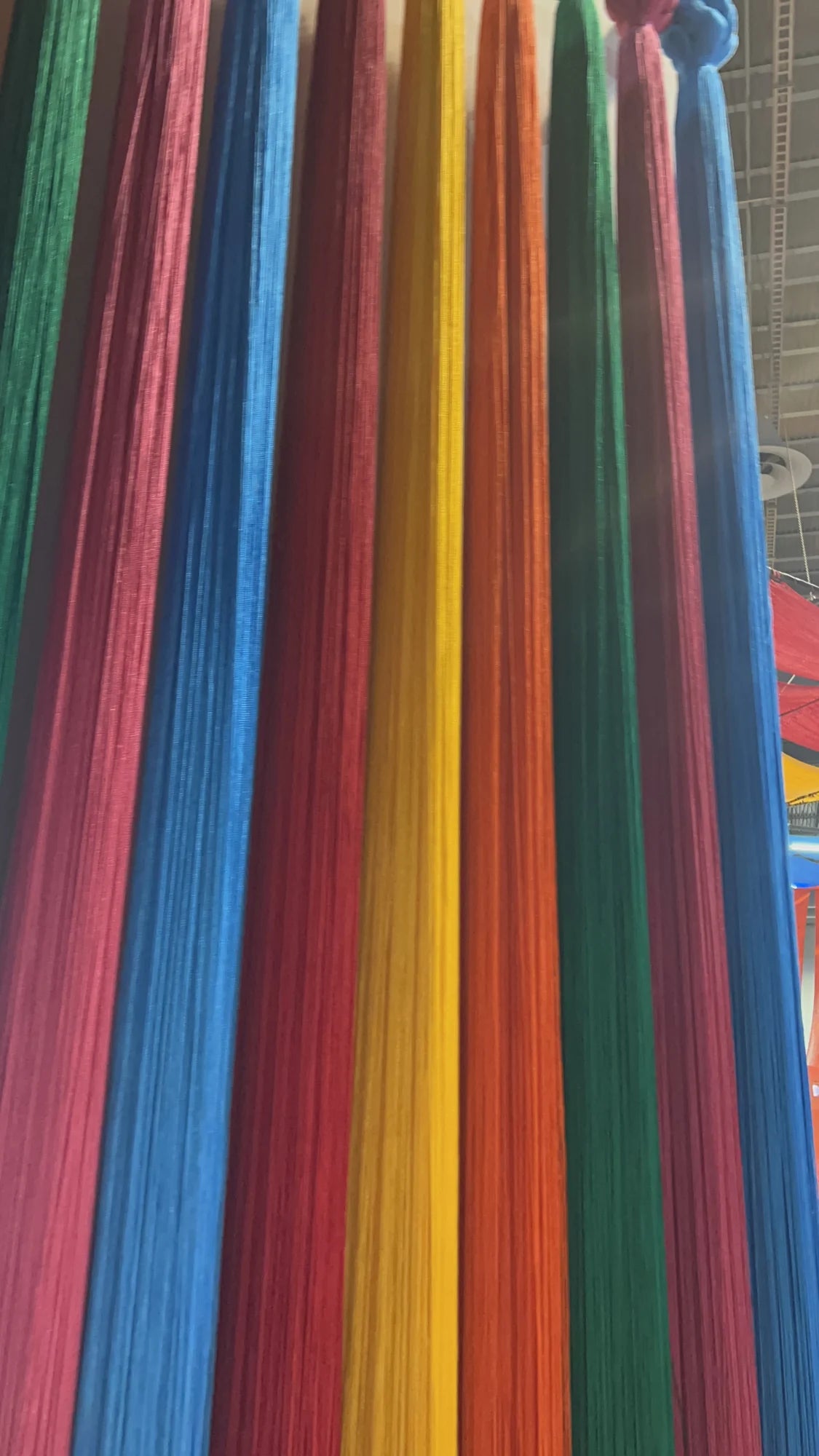 Detalle de hilos verticales en verde, rosa, azul, amarillo y naranja, con nudos en la parte superior.